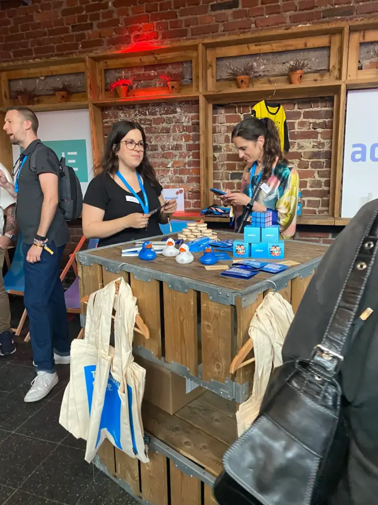 Zwei Damen im zweiten Stand auf der koks.digital 2025, die kleine Geschenke verteilen.