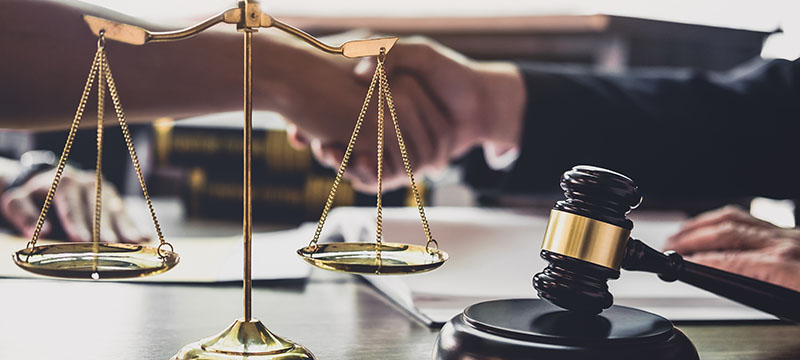 Händeschütteln nach erfolgreicher rechtlicher Beratung mit Waage und Richterhammer im Vordergrund
